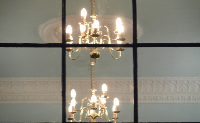 ashburton-chapel-light Brass chandaliers viewed through a window